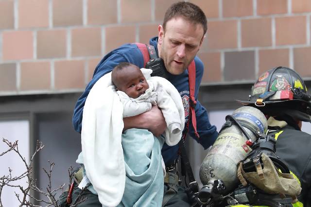 A firefighter carrying a rescued infant wrapped in a blanket